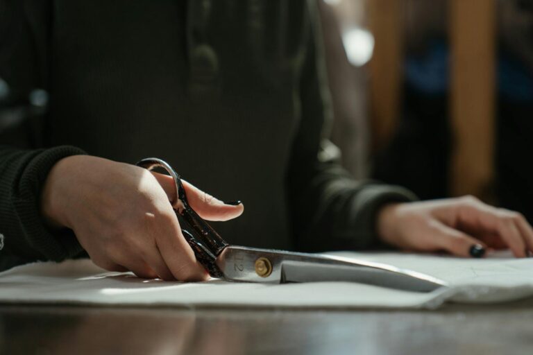 Close-up of a&nbsp;tailor's hands cutting fabric with scissors, emphasizing craftsmanship and skill.